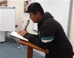 Students leans on podium while reciting a poem into a microphone. 